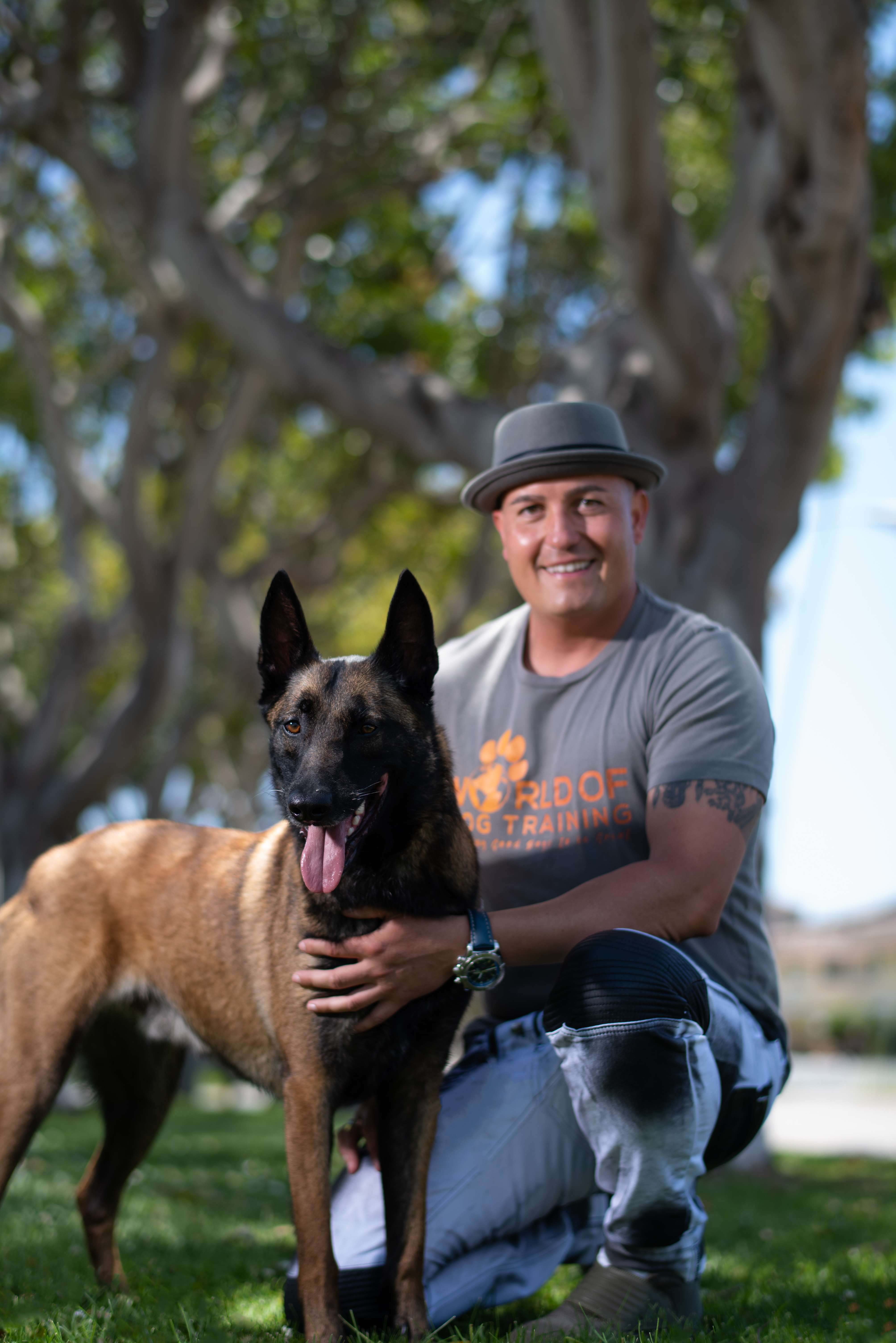 Ryan Matthews, U.S. Army veteran and founder of World of Dog Training, kneeling with his Belgian Malinois under a tree in Orange County